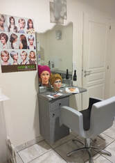 Fauteuil de salon de coiffure gris placé face à un miroir avec 2 têtes de mannequins, une avec une perruque et l'autre avec un turban