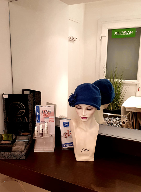 Grand miroir avec une tête à perruque portant un turban bleu avec une fleur cousue dessus et, à côté, des vernis de la marque Eye Care Cosmetics