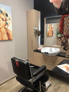 salon de coiffure avec un fauteuil noir face à un miroir avec des turbans accrochés à droite du miroir