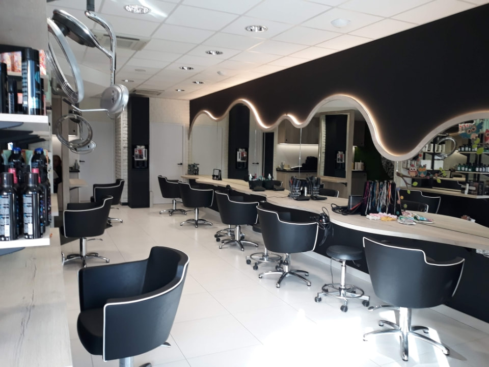 Salon de coiffure avec plusieurs sièges noirs face un grand miroir faisant toute la longueur du mur